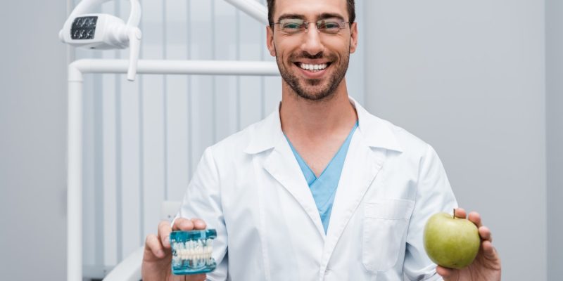 cheerful-dentist-in-glasses-holding-tooth-model-an-2024-11-14-14-14-01-utc
